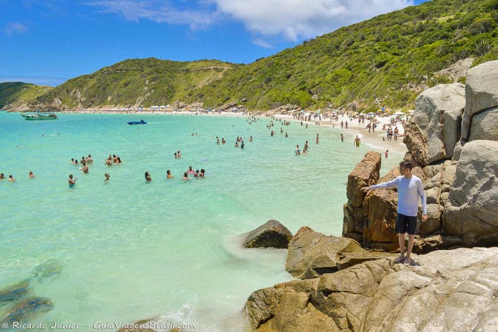 Imagem de um menino em pé nas pedras da Praia Pontal do Atalaia.